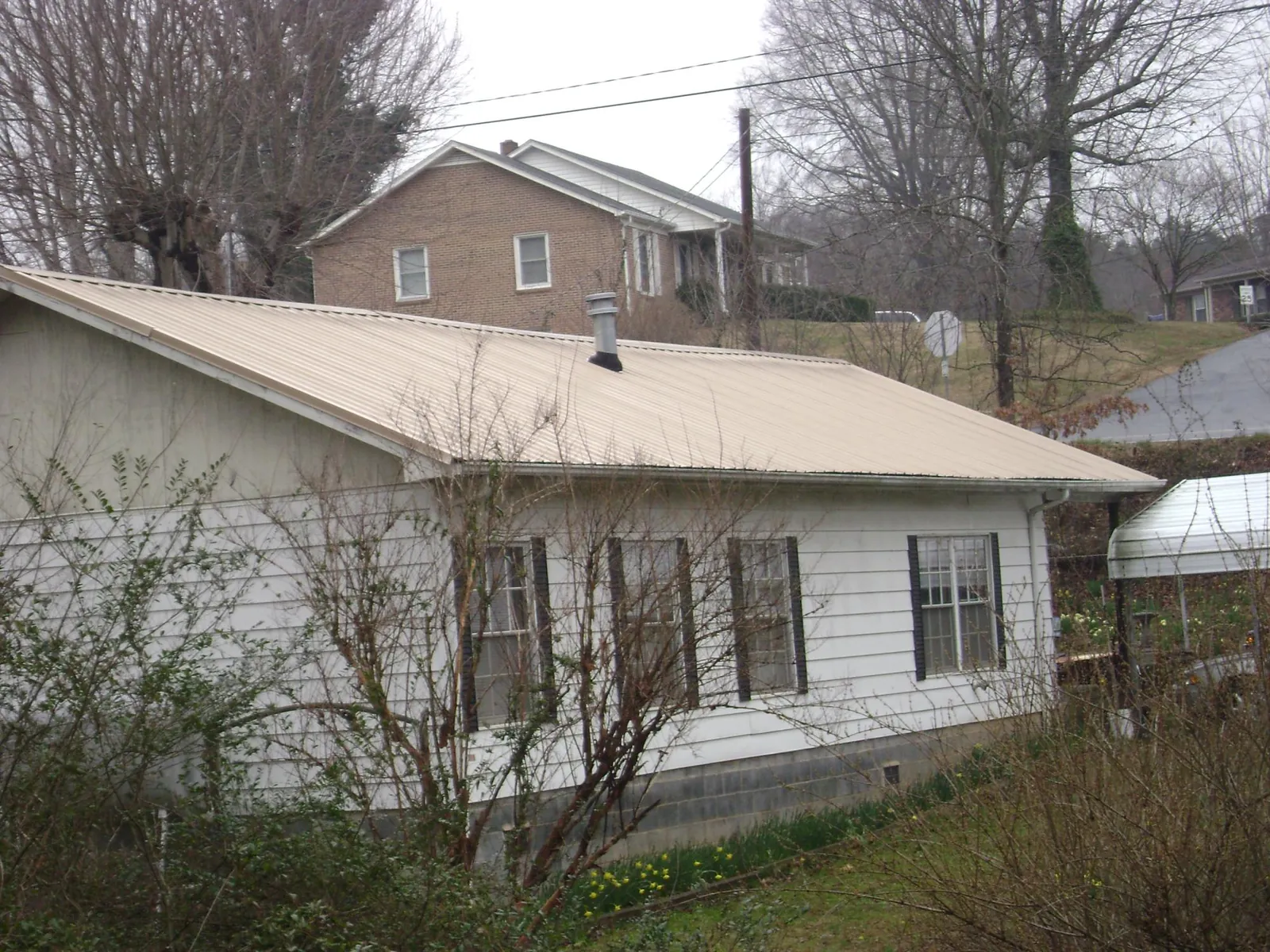 Tan metal roof on a white sided house set into a hillside — Commercial Roofing by Roofing Brothers in Hyde Park